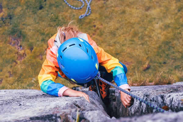 una niña subiendo una pared con arnés y casco
